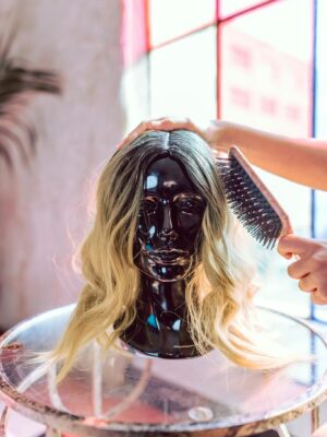 A fashionable blonde wig being styled on a black mannequin head indoors.