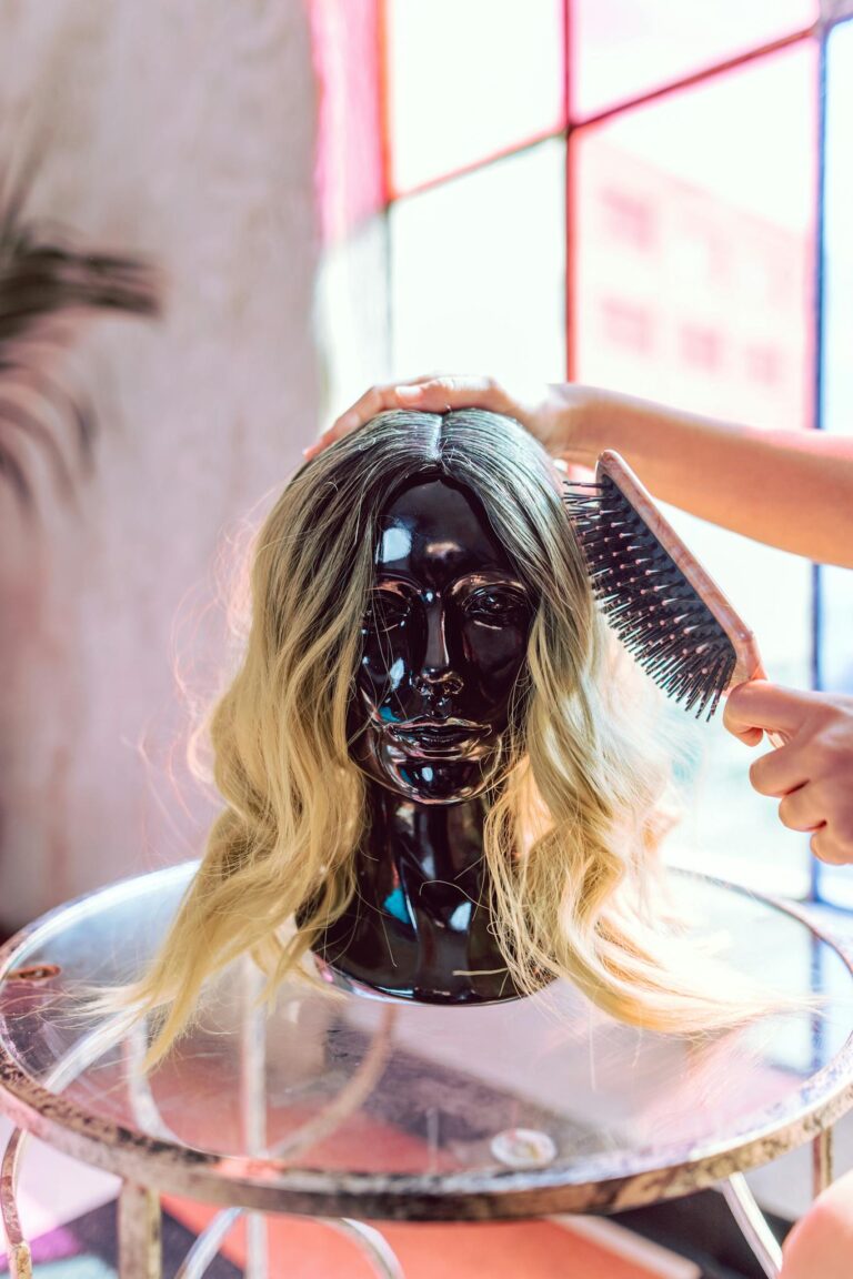 A fashionable blonde wig being styled on a black mannequin head indoors.