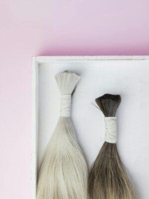 Top view of two hair extensions tied in bundles against a pink background.