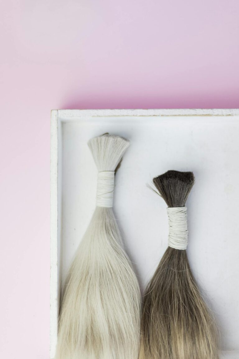 Top view of two hair extensions tied in bundles against a pink background.